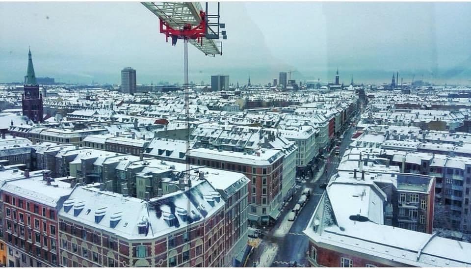 En tårnkran, der rager op over et bylandskab dækket af sne, set i fugleperspektiv.